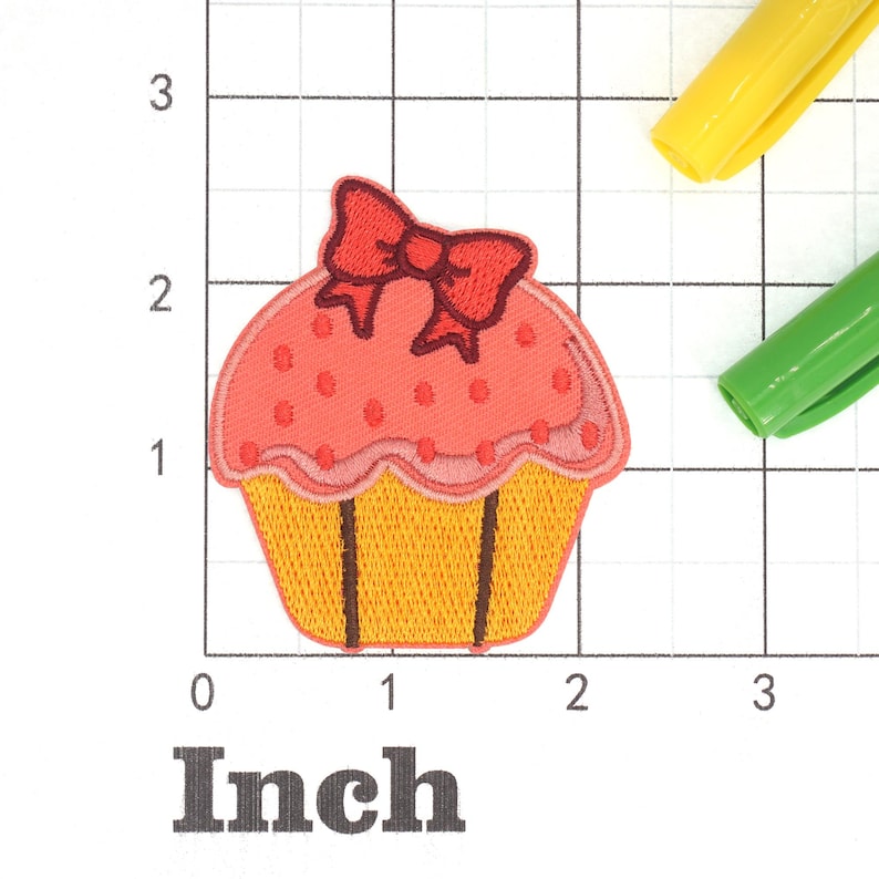 Może przedstawiać: R&oacute;żowo-ż&oacute;łty cupcake z czerwoną kokardką na g&oacute;rze. Cupcake jest ozdobiony białymi kropkami. Cupcake ma około 5 cm szerokości.
