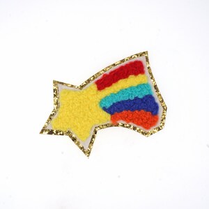 Könnte beinhalten: Ein gelber sternförmiger Patch mit einem Regenbogenstreifenmuster, das mit goldenem Glitzer umrandet ist.
