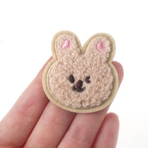 May include: A beige fuzzy bunny patch with pink ears and a brown embroidered face.