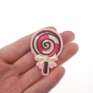 May include: Pink felt iron-on patch with an embroidered brown and pink swirl lollipop design.