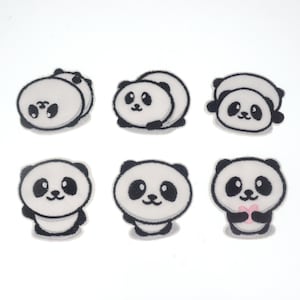 Pode incluir: Seis patches de urso panda em várias poses. Os pandas são brancos com detalhes em preto, incluindo suas orelhas, olhos e marcas. Um panda segura um coração rosa. Os patches são provavelmente para roupas ou artesanato.