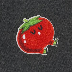 Puede incluir: Tomate de fieltro rojo con un tallo verde y una linda carita de dibujos animados. El tomate tiene dos ojos y una peque&ntilde;a boca.