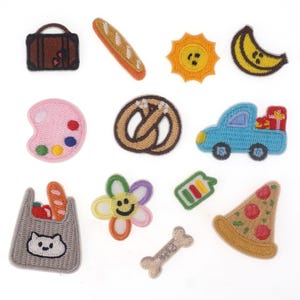 Può includere: Un set di 12 toppe ricamate colorate da stirare, con vari disegni, tra cui un sole, un pretzel, un fiore, una fetta di pizza, un'auto, una banana, una baguette, una tavolozza di colori, un osso, una valigia, una borsa della spesa e una batteria.
