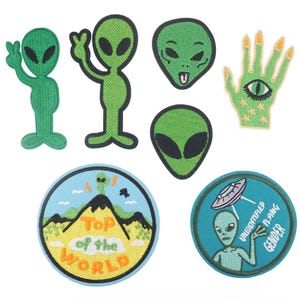 May include: Set of eight embroidered iron-on patches featuring alien and space-themed designs. The patches include a green alien with a peace sign, a green alien with a tongue sticking out, a green alien head, a green hand with an eye, a green alien head with a UFO, a green alien on a mountain with the text "Top of the World", and a blue alien with a UFO and the text "Unidentified Flying Gender".