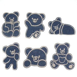 Puede incluir: Seis parches bordados para planchar que representan osos de dibujos animados en varias poses. Los osos están delineados en blanco y rellenos de un color azul vaquero.