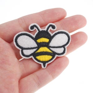 May include: An embroidered bee patch in yellow and black with white wings. The bee is cartoon-style and has a simple design.