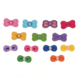May include: Assortment of 13 colorful embroidered iron-on bow patches. The bows are in various colors including pink, blue, green, yellow, purple, and orange.