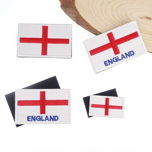 May include: A collection of rectangular patches featuring the England flag design: a red cross on a white background. Some patches have the word "ENGLAND" in blue. Patches are of different sizes and are displayed on a white surface.