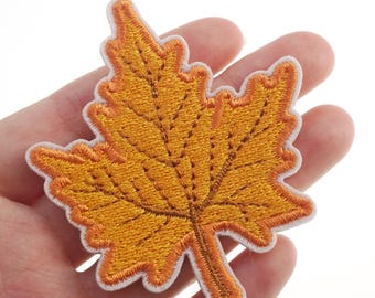 Può includere: Un toppa ricamata a forma di foglia d'acero gialla con un contorno bianco. La toppa è perfetta per aggiungere un tocco autunnale a vestiti, borse o artigianato.