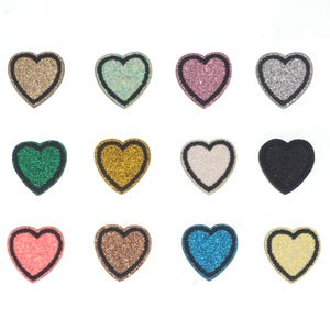 Può includere: Dodici toppe a forma di cuore con contorni neri. Le toppe sono realizzate in tessuto glitterato in vari colori, tra cui oro, argento, rosa, blu, verde e nero.