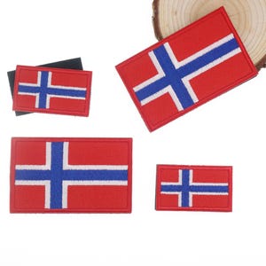 May include: A collection of red, white, and blue Norwegian flag patches in various sizes. The patches feature a red background with a white-bordered blue cross design, representing the flag of Norway. The patches are rectangular.