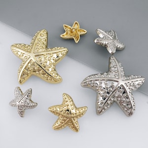 Puede incluir: Colección de estrellas de mar metálicas en tonos dorados y plateados. Las estrellas de mar, de varios tamaños, tienen una superficie texturizada con pequeños puntos en relieve. La disposición incluye estrellas de mar grandes y pequeñas.
