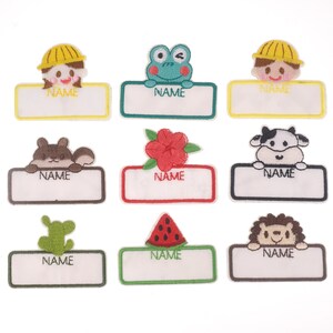 Puede incluir: Nueve parches termoadhesivos coloridos con diferentes personajes de dibujos animados y la palabra "NAME" sobre un fondo blanco. Los personajes incluyen una rana, una vaca, una ardilla, una flor, una sandía, un erizo y dos personas con gorras de construcción.