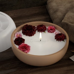May include: A brown ceramic bowl candle with a white wax top and a lit wick. The candle is decorated with pink and burgundy flowers.