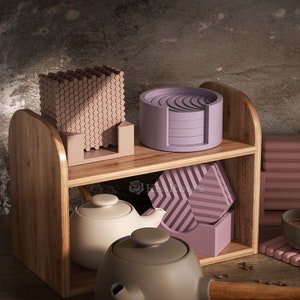 May include: A wooden shelf with two tiers displays a selection of coasters. The top tier features a stack of round, purple coasters and a stack of square, brown coasters. The bottom tier holds a stack of square, purple coasters and two ceramic teapots, one white and one grey.