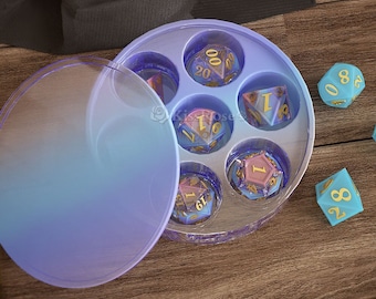 May include: A clear plastic container with a lid, containing seven iridescent dice with gold numbers. The dice are in a circular pattern, with each die in its own compartment. The container is on a wooden surface.