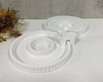 May include: White ceramic reindeer figurine with a ring-shaped base. The base has a textured edge and a smaller ring in the center. The reindeer is standing on the larger ring.