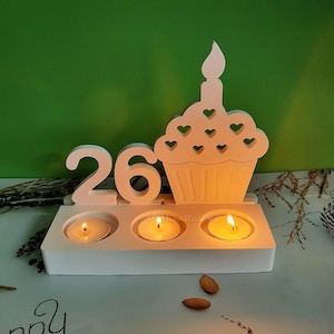 Puede incluir: Portavelas de madera blanco con el número 26 y un diseño de cupcake. El portavelas tiene tres ranuras para velas y cada ranura tiene una vela de té encendida.