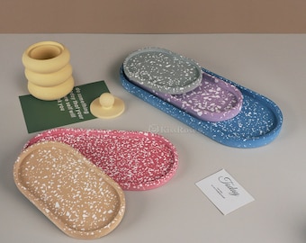 May include: Four oval-shaped trays with speckled patterns in blue, purple, pink, and beige. The trays are made of concrete and have a rustic, handmade look.