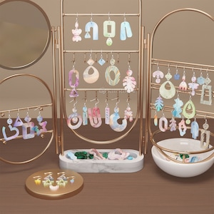 May include: A gold metal earring display stand with multiple tiers of hooks holding colourful, abstract, and geometric resin earrings. The stand has a marble base and a bowl for storing loose earrings.