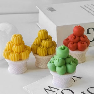 Könnte beinhalten: Drei kleine weiße Körbe gefüllt mit Miniatur-Obst- und Gemüseformen. Die Körbe sind gefüllt mit gelben Kürbissen, roten Äpfeln und grünen Äpfeln.