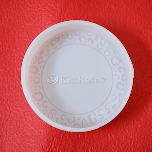 May include: White plastic lid with a decorative pattern around the edge. The pattern is made up of small, repeating shapes.