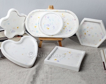 May include: Five white ceramic trays with a speckled pattern in shades of pink, blue, and yellow. The trays are in various shapes, including a heart, a star, a rectangle, and two octagons.