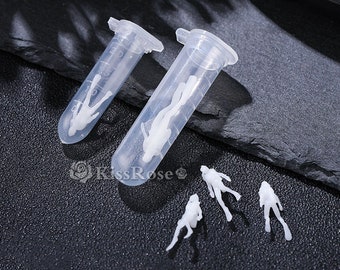 Op de afbeelding: Vier witte plastic figuurtjes van duikers in verschillende poses, waarvan er twee in doorzichtige plastic buizen met schroefdeksels zitten.