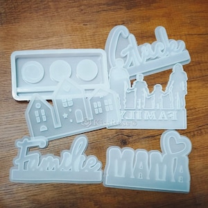 Puede incluir: Un conjunto de cinco moldes de silicona blanca para manualidades. Los moldes presentan las palabras "Abuela", "Familia", "Mamá", "Bienvenida" y una casa con tres ventanas. Los moldes están diseñados para crear manualidades de resina.