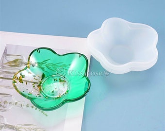 May include: A green resin dish with gold leaf accents in the shape of a five-pointed star. The dish is sitting on a white surface next to a clear silicone mold of the same shape.