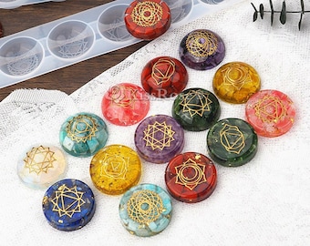 May include: Set of seven chakra stones with gold symbols on a white background. The stones are arranged in a circle and are in the colors of the chakras: red, orange, yellow, green, blue, indigo, and violet.