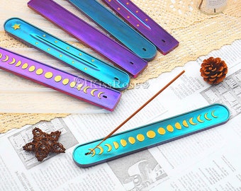 May include: Set of five iridescent incense holders with different celestial designs. The holders are made of metal and have a smooth, polished finish. Each holder features a unique design, including stars, moons, and a crescent moon.