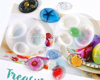 Puede incluir: Un juego de moldes de silicona transparente para hacer joyas de resina. Los moldes tienen forma de lágrima y tienen un agujero en la parte superior para colgar. Hay seis moldes en total, y están dispuestos en dos filas de tres. Los moldes están rodeados de una variedad de piezas de resina de colores, incluyendo una estrella de mar azul, una piedra verde y una flor roja.
