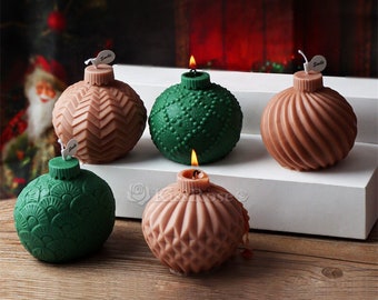 May include: Five decorative Christmas ornament candles in green and brown. The candles are shaped like baubles and have different textures. Some of the candles are lit.