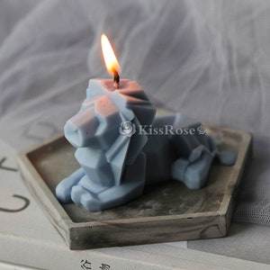 May include: A blue geometric lion candle with a lit wick. The candle is sitting on a gray hexagonal tray.