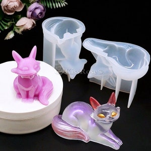 May include: Two clear silicone molds for making resin crafts. The molds are shaped like a sitting fox and a lying fox. The molds are shown with finished resin crafts in pink and purple.