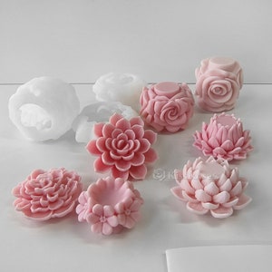 Könnte beinhalten: Ein Set aus rosa und weißen Silikonformen zum Herstellen von blumenförmigen Kerzen oder Seife. Die Formen haben die Form von Rosen, Lotusblumen und Sukkulenten.