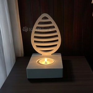 May include: White wooden candle holder shaped like a teardrop with a small candle burning inside. The holder has a decorative design of horizontal lines.