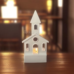 May include: White ceramic church-shaped candle holder with a small candle inside. The candle holder is on a wooden surface.