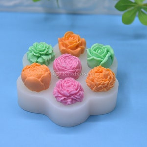 May include: A white silicone mold with seven different flower shapes. The mold is filled with colorful fondant flowers in shades of green, orange, pink, and red.