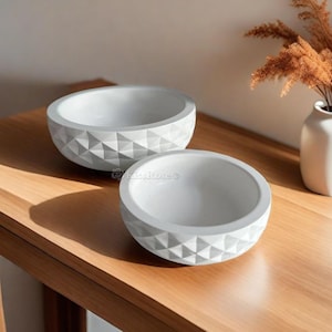 May include: Two white concrete bowls with a geometric pattern on a wooden surface. The bowls are different sizes and are perfect for displaying decorative items or serving snacks.