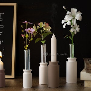 Könnte beinhalten: Vier weiße Keramikvasen mit verschiedenen Blumenarrangements. Die Vasen stehen auf einer Holzoberfläche. Die Blumen sind rosa, weiß und grün. Vorne steht eine weiße Kerze.