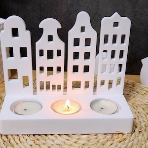 May include: White wooden candle holder shaped like a row of houses with three candle slots. The holder is on a woven straw surface.