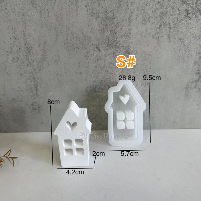 May include: Two white silicone molds shaped like houses with a heart and windows. The larger mold is 9.5 cm tall and 5.7 cm wide. The smaller mold is 8 cm tall, 4.2 cm wide, and 2 cm deep. The molds weigh 28.8 grams.