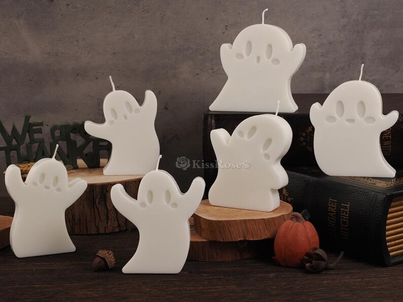 Op de afbeelding: Set witte kaarsen in de vorm van een spook. De kaarsen staan op een houten oppervlak met een boek op de achtergrond.