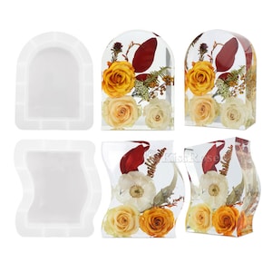 Könnte beinhalten: Drei transparente Harzformen zum Herstellen von Blumenarrangements. Die Formen sind in Form eines Bogens, einer Welle und eines Rechtecks. Die Formen werden mit getrockneten Blumen darin gezeigt.