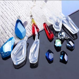 以下が含まれることがあります： ジュエリーを作るための透明なシリコンモールドのセット。モールドは涙滴型のクリスタル形をしています。青と赤の完成したレジン作品もいくつかあります。