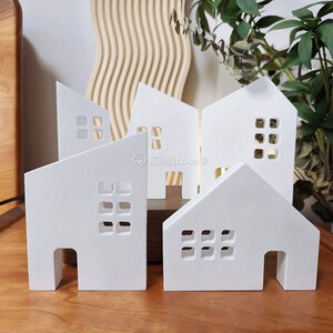 May include: Five white wooden houses with cut-out windows and doors. The houses are arranged in a row on a wooden surface.