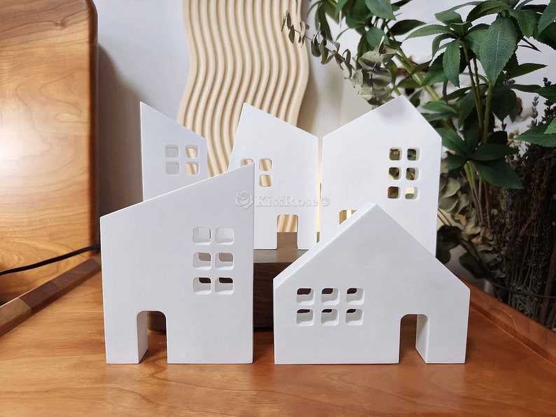 May include: Five white wooden houses with cut-out windows and doors. The houses are arranged in a row on a wooden surface.