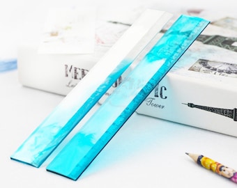 May include: Two clear plastic rulers with a blue and white marbled design. The rulers are 12 inches long and have black markings.